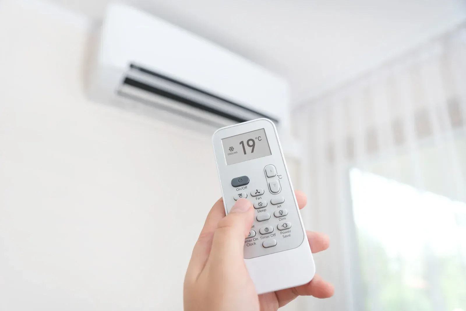 A person is holding a remote control in front of an air conditioner.