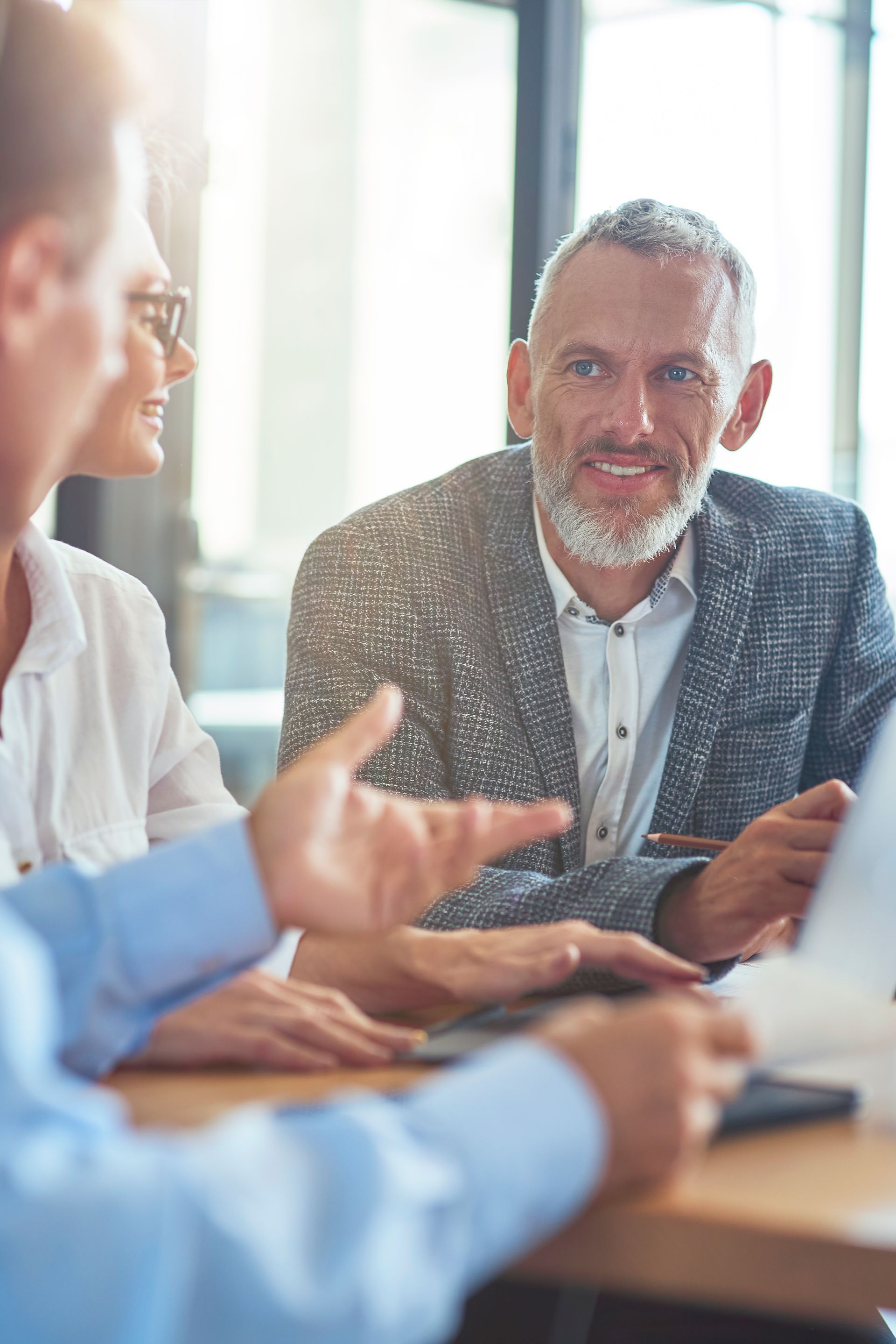 A team collaborates in an office, with one person speaking while looking toward a colleague at a desk.
