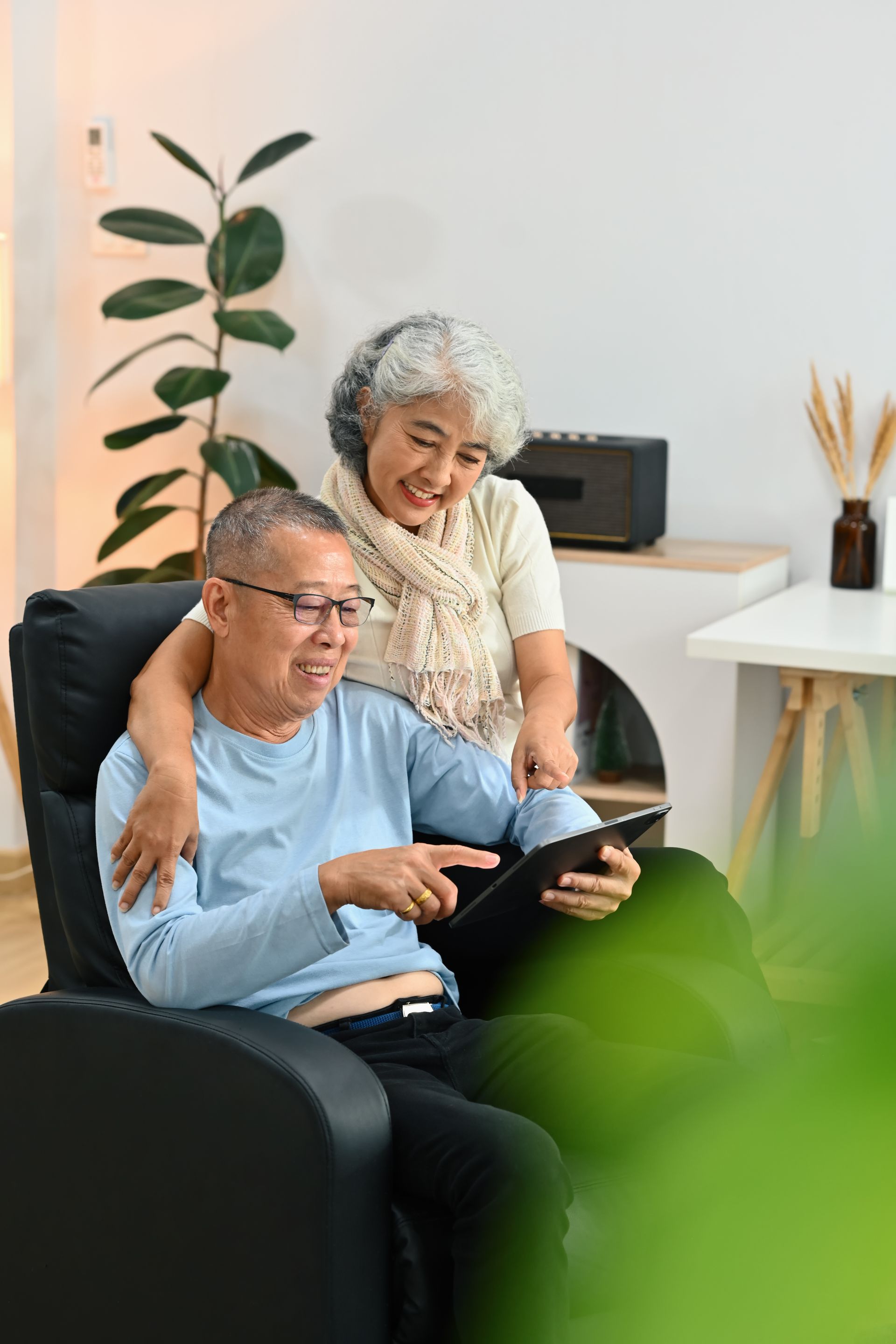 Two people sitting in a black recliner, smiling while looking at a tablet together in a bright, modern living room.