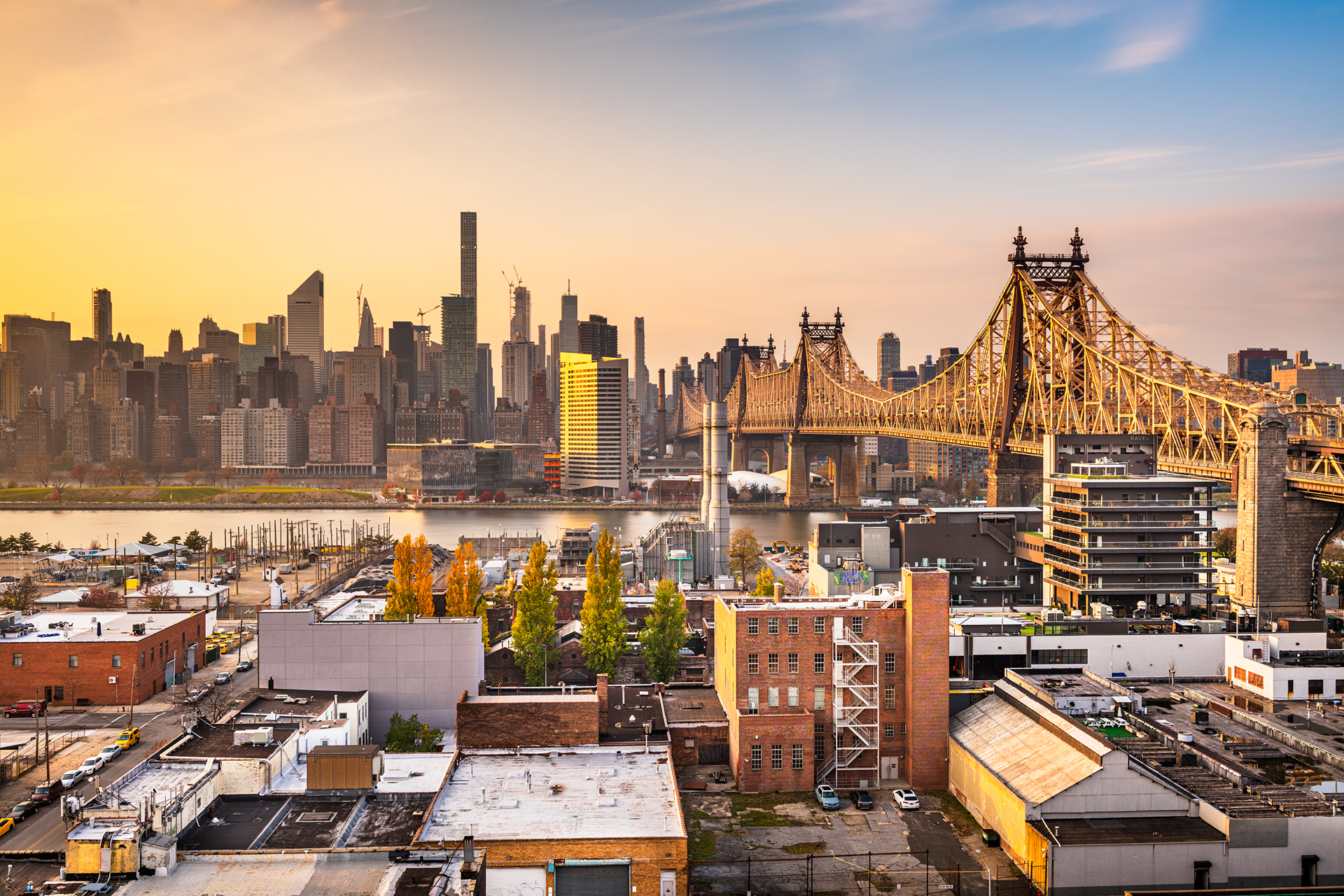 Queensboro Bridge spans the East River at sunset with the New York City skyline in the background.