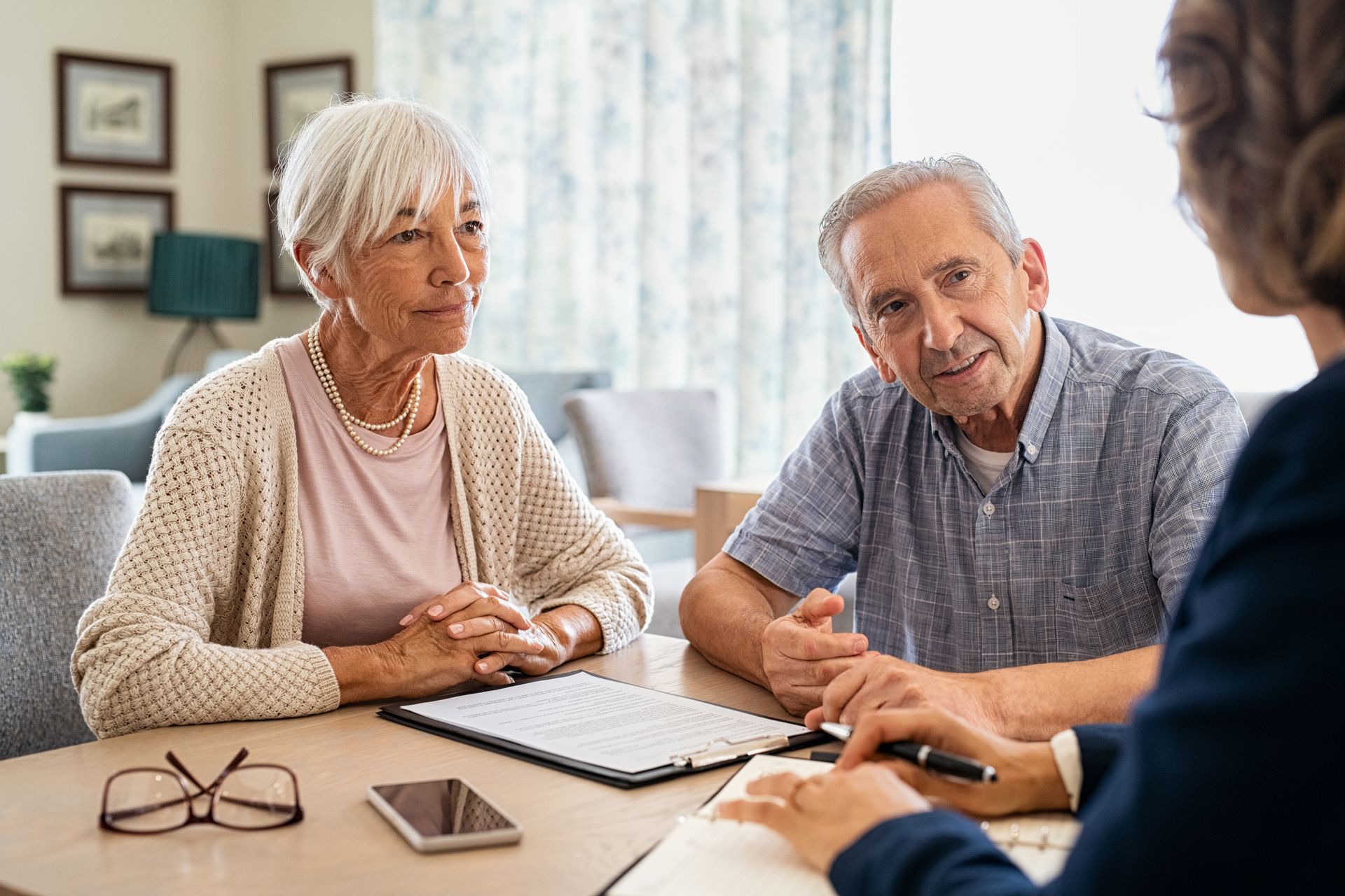 Two people sit at a table across from an advisor, listening as they review paperwork in a well-lit office.