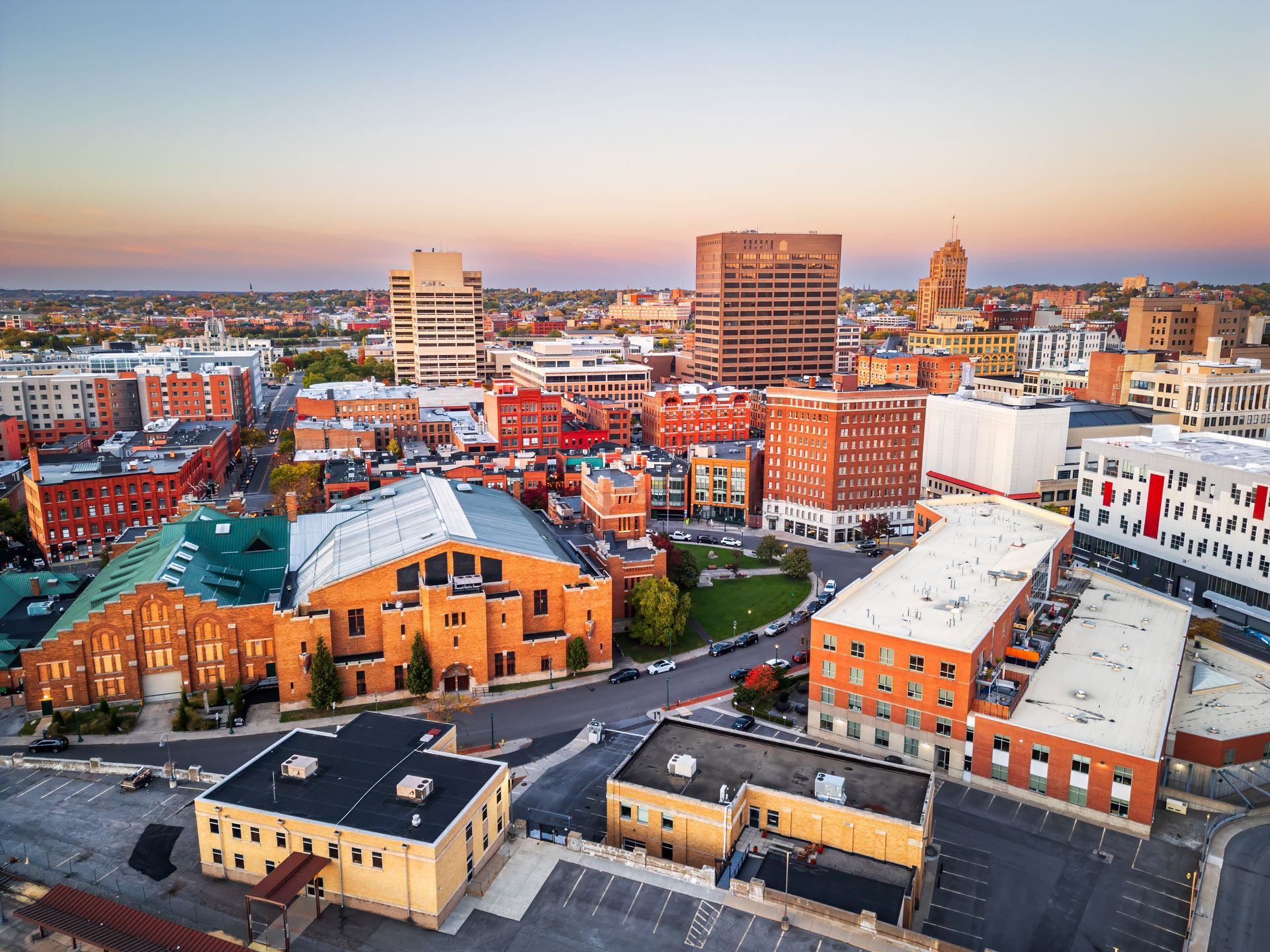 Aerial view of an urban cityscape at sunset, featuring a mix of brick and modern buildings under a clear sky.