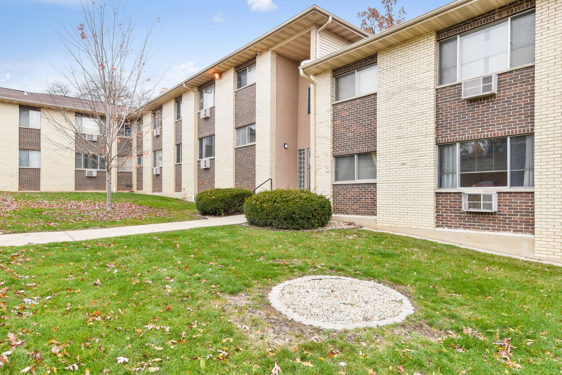 A brick apartment building with a lush green lawn in front of it.