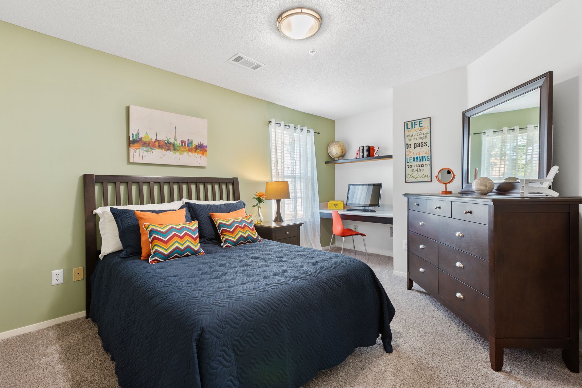A bedroom with a bed , dresser , desk and mirror.