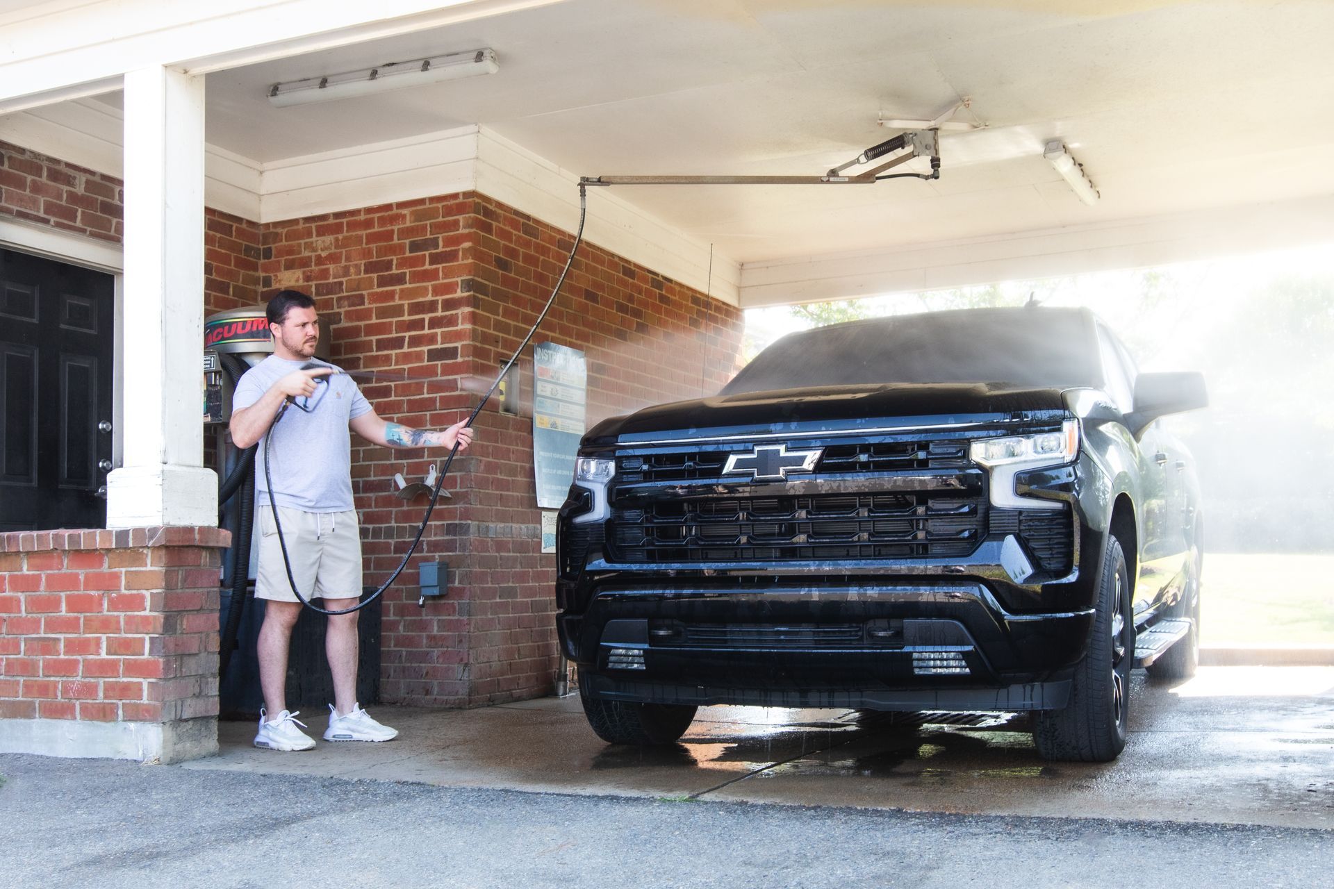 A man is washing a black truck in a garage.