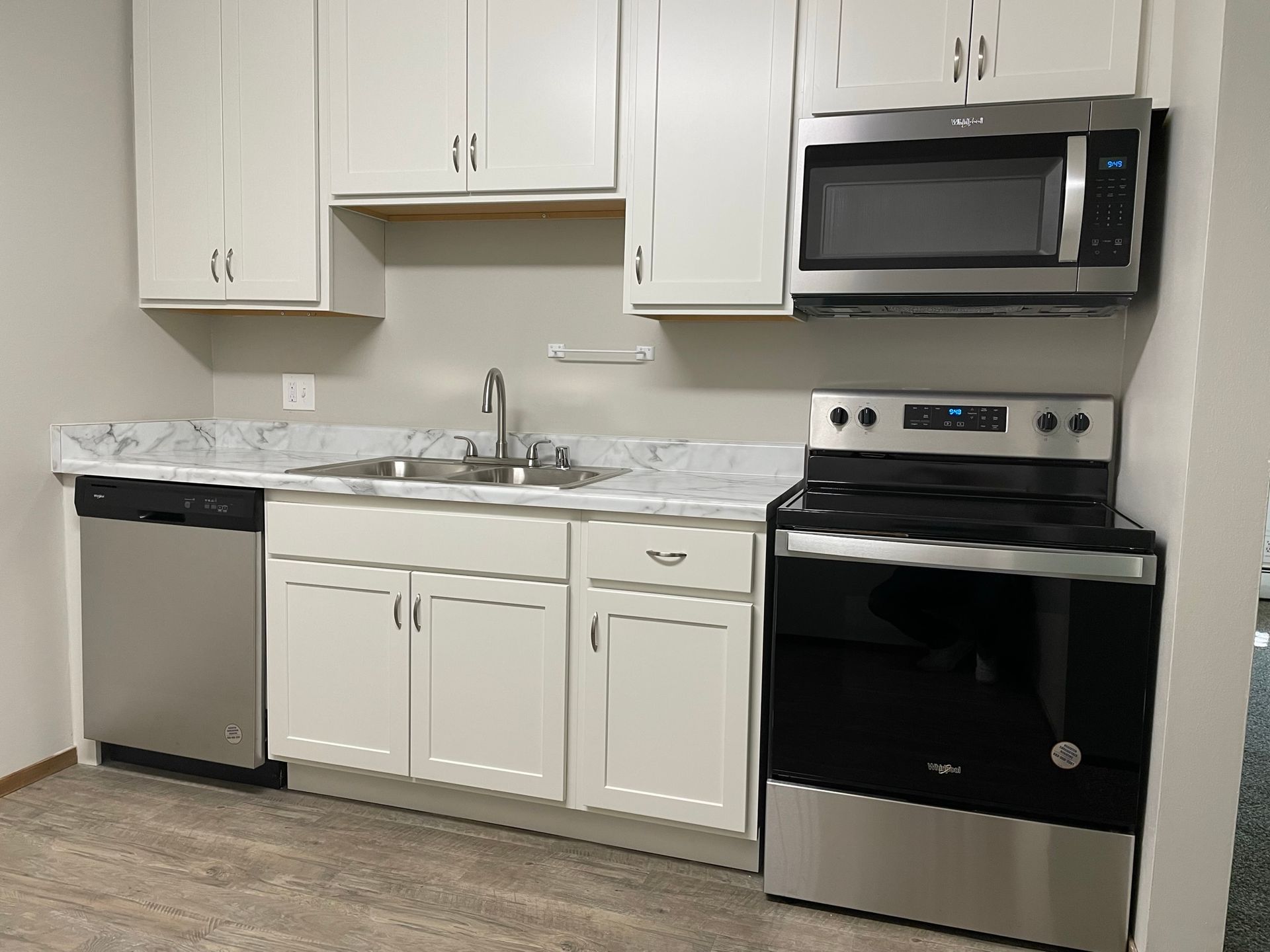 A kitchen with white cabinets , stainless steel appliances , a sink , stove and microwave.