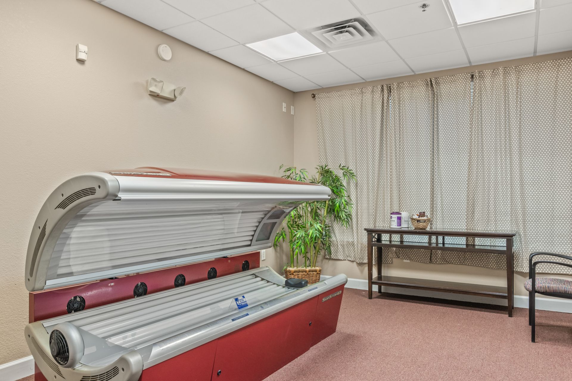 A red tanning bed is sitting in a room next to a window.