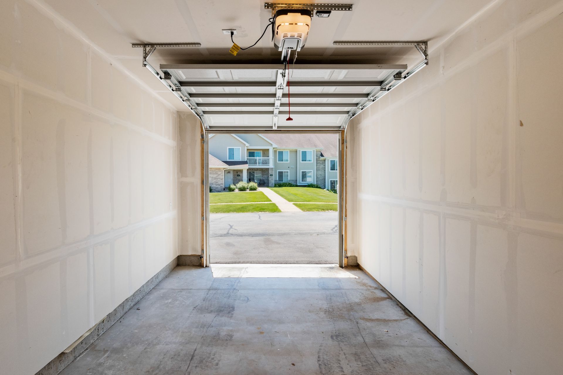 An empty garage with the door open and a house in the background.