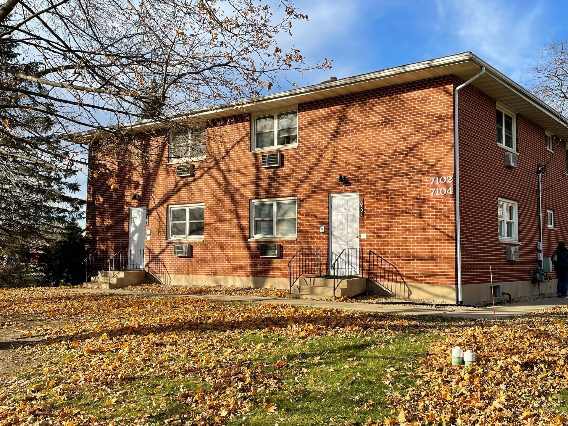 A brick apartment building with a lot of leaves on the ground in front of it.