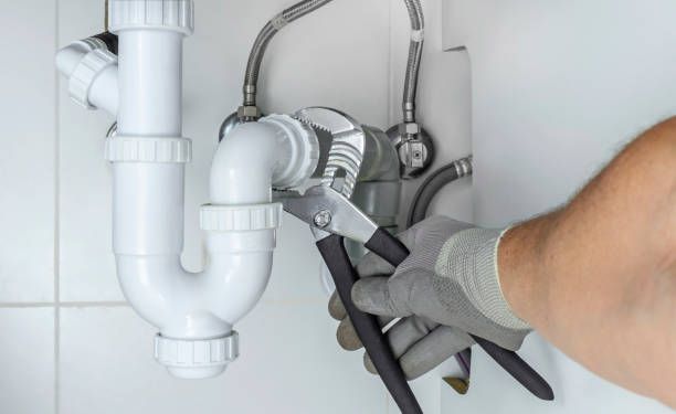 Plumber repairing white P-trap pipe under sink.