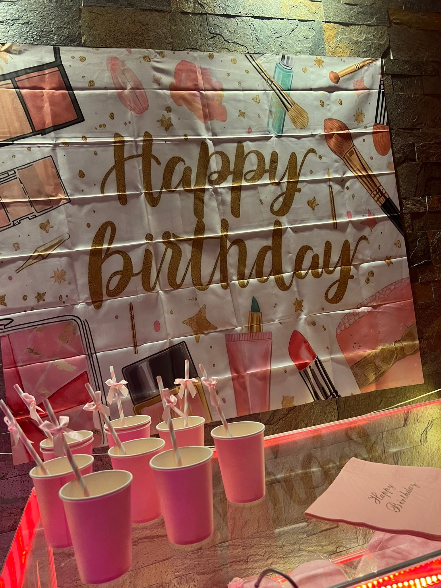 Uno striscione di buon compleanno con bicchieri rosa e cannucce su un tavolo.