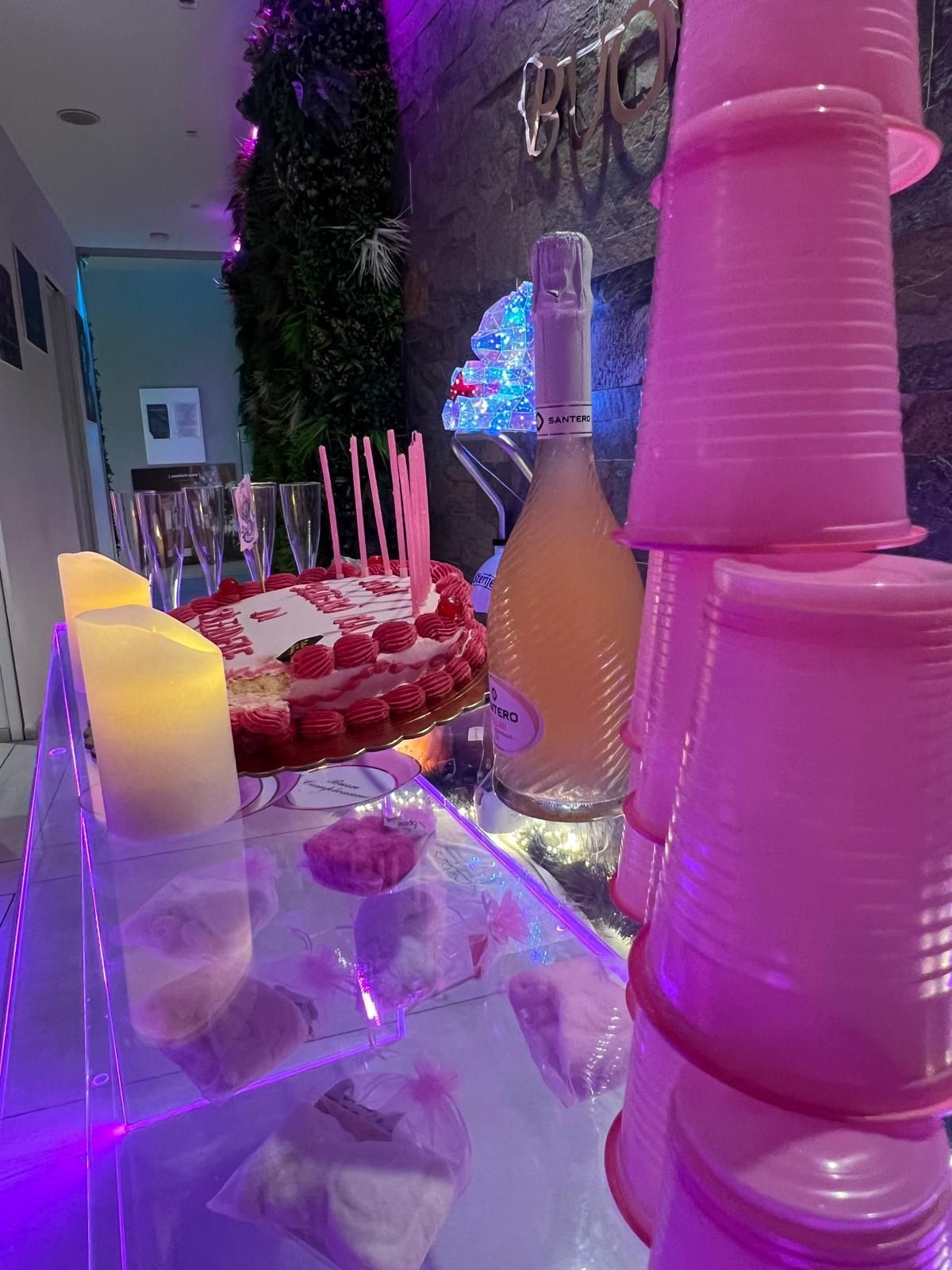 Un tavolo con una torta, delle candeline e delle tazze rosa impilate l'una sull'altra.