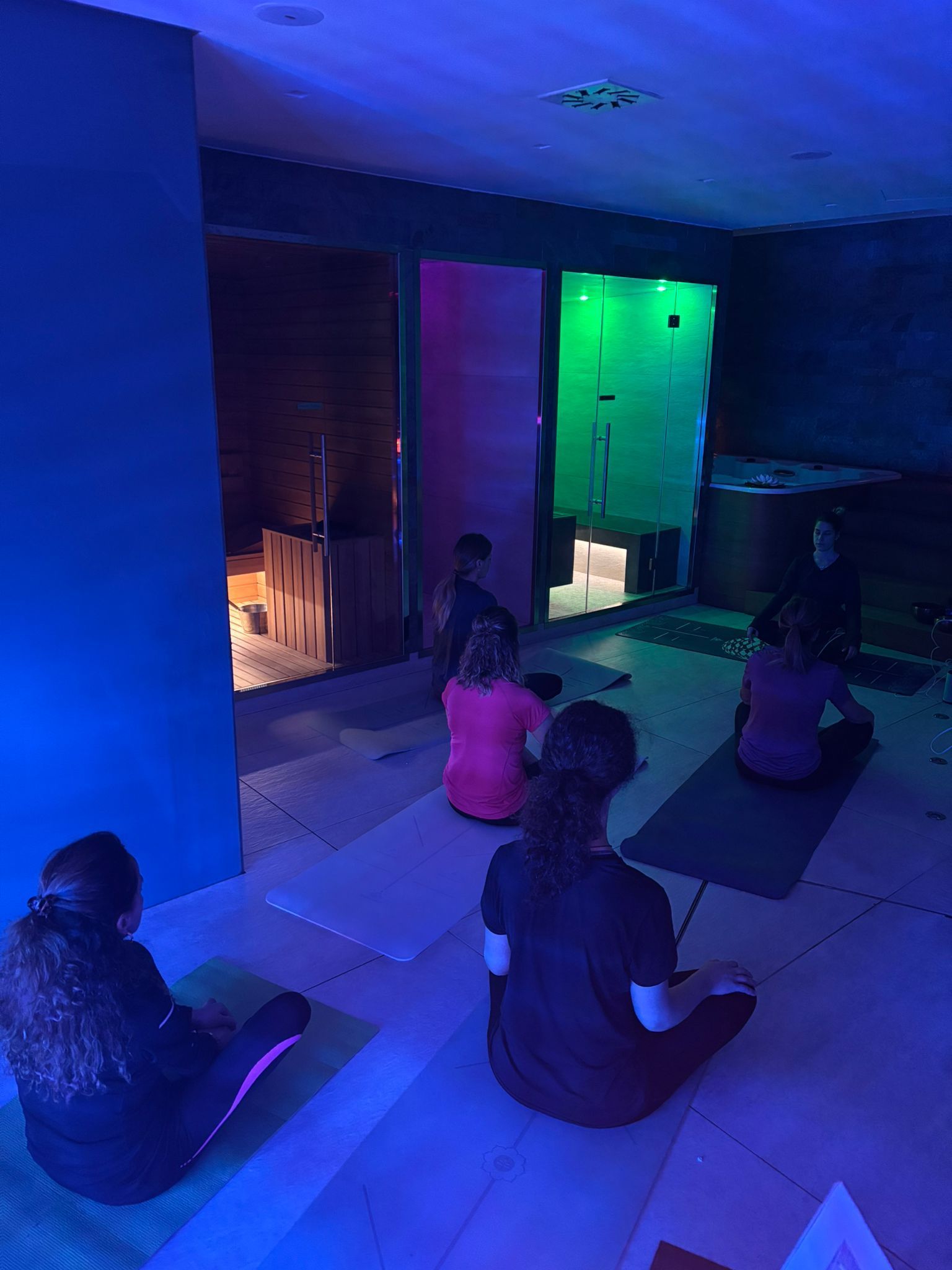 Un gruppo di persone è seduto su tappetini da yoga in una stanza buia.