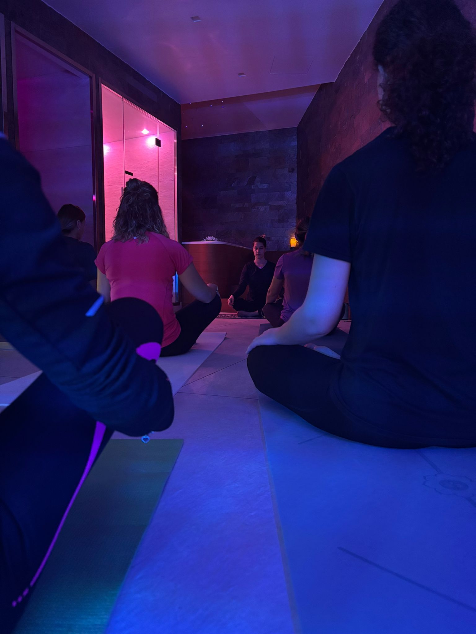 Un gruppo di persone è seduto su tappetini da yoga in una stanza buia.
