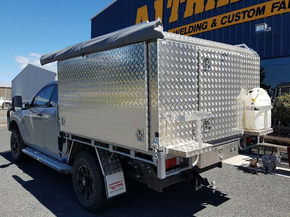 A silver truck with a canopy on top of it is parked in front of a building.
