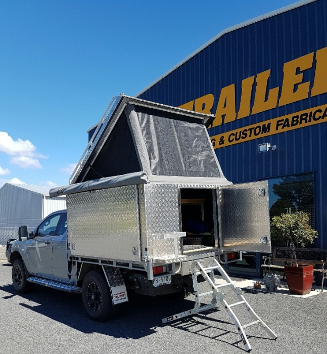 A truck is parked in front of a building that says trailers & custom fabrication