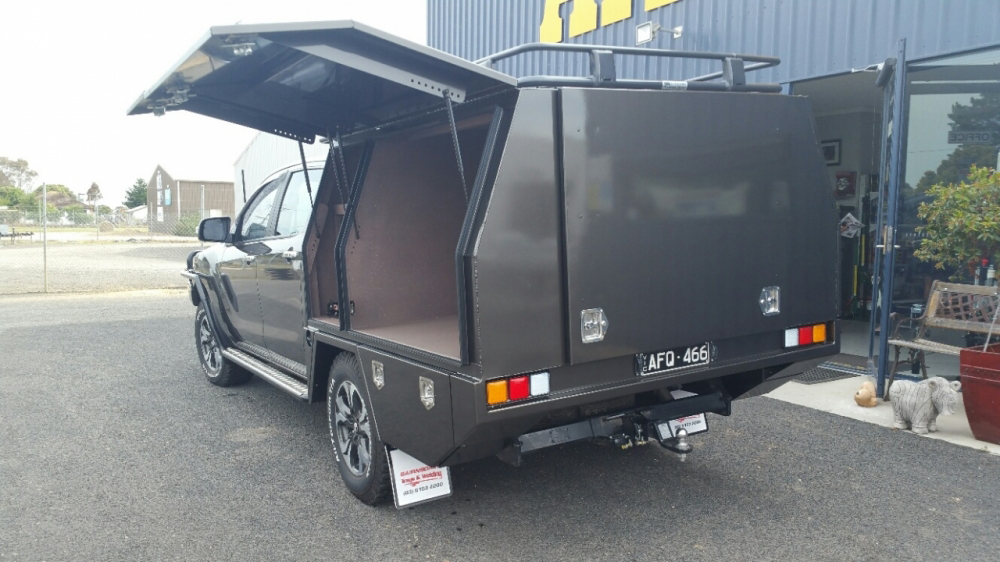 A black truck with a canopy on top of it is parked in front of a building.