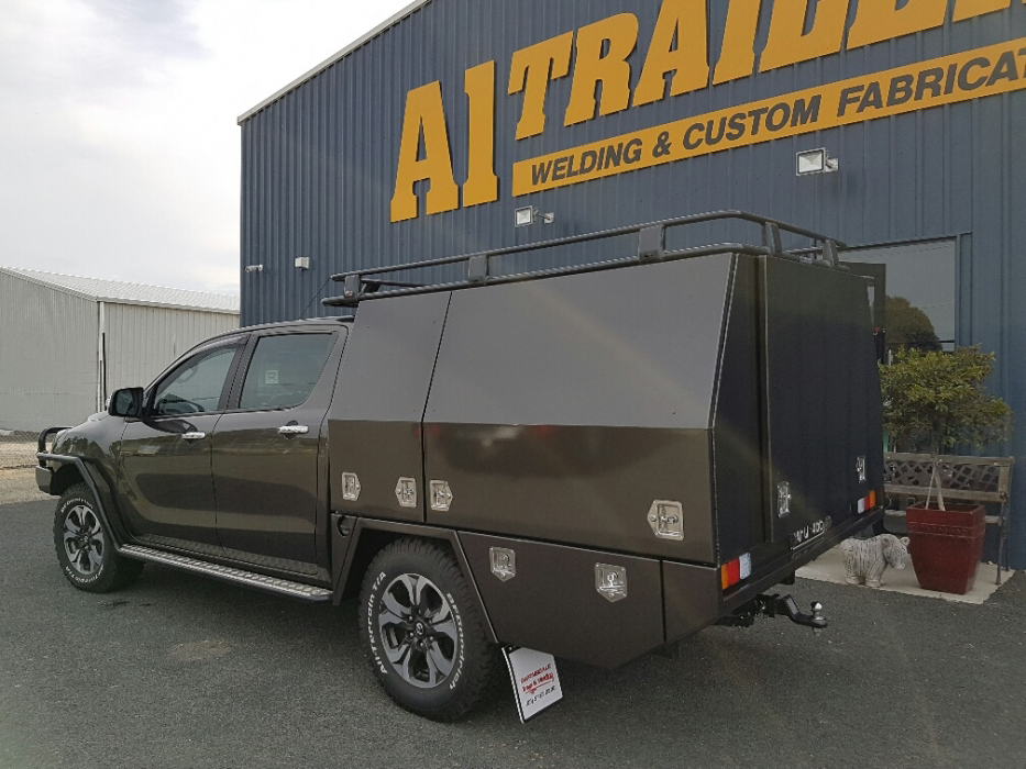 A truck with a canopy is parked in front of a building that says welding and custom fabrication.