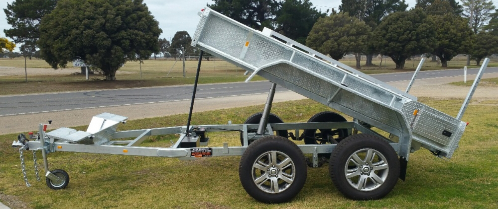 A dump trailer is parked on the grass next to a road.