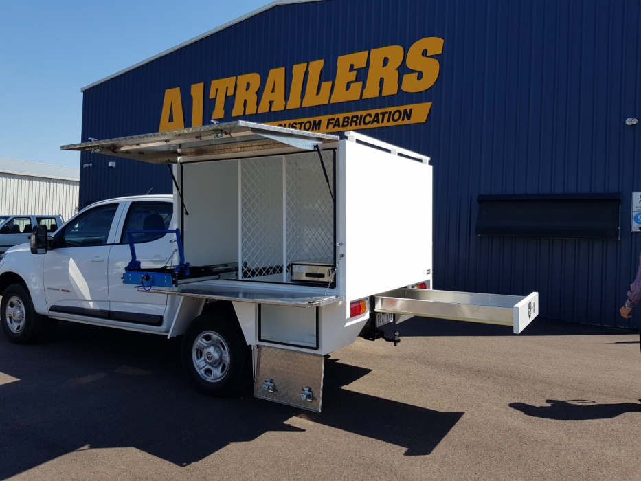 A white truck with a trailer attached to it is parked in front of a trailers building.