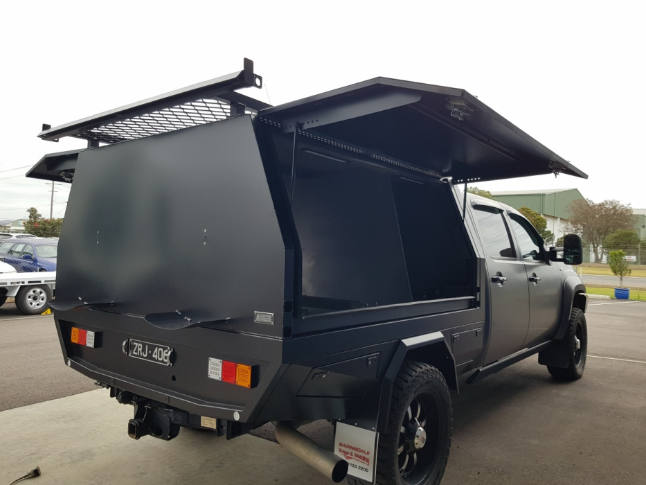 A black truck with a canopy on top of it is parked in a parking lot.