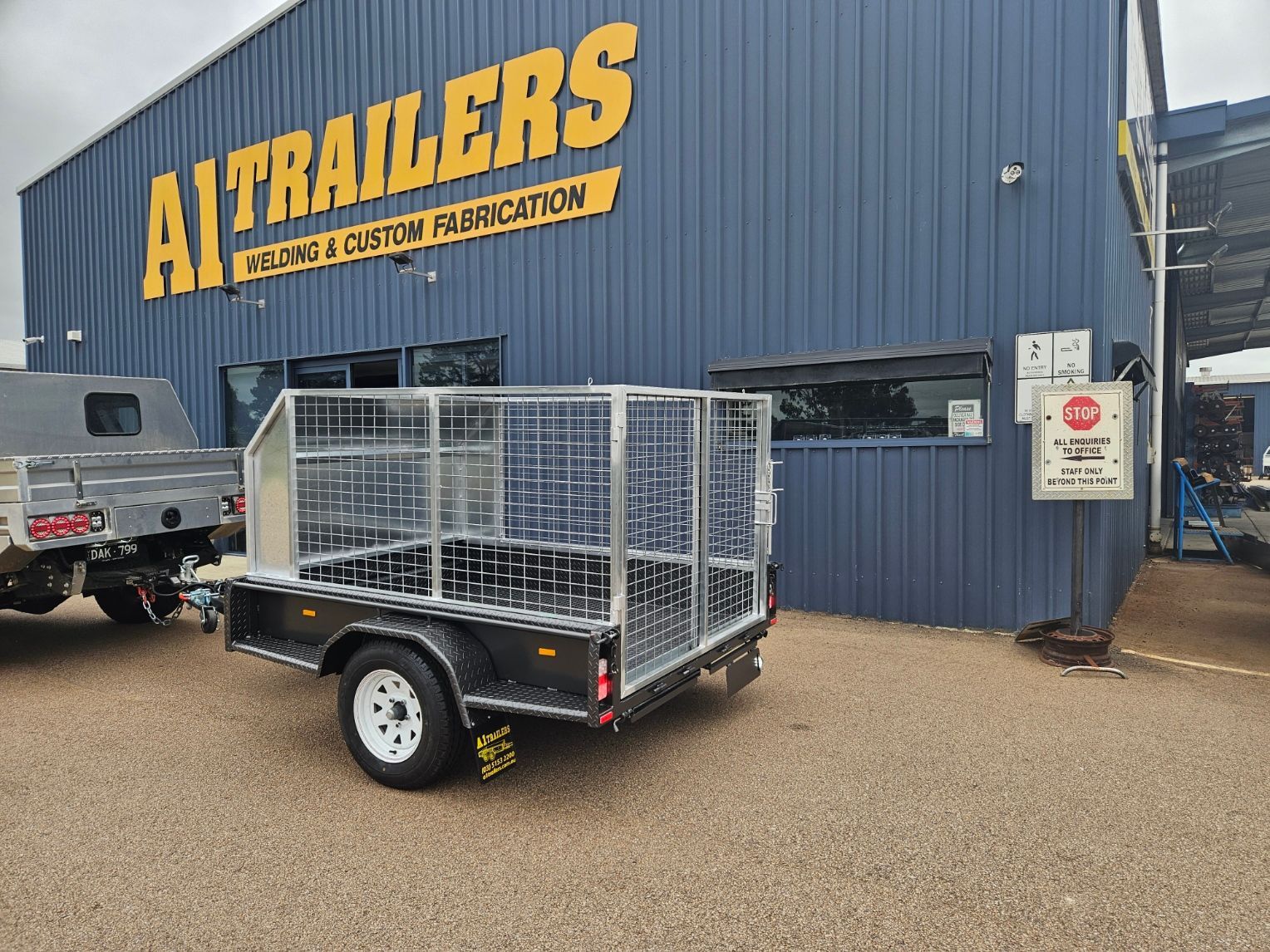 A white truck is parked in front of a building that says ai trailers welding and custom fabrication.