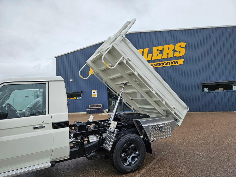 A white tipper truck is parked in front of a building with the tray up.