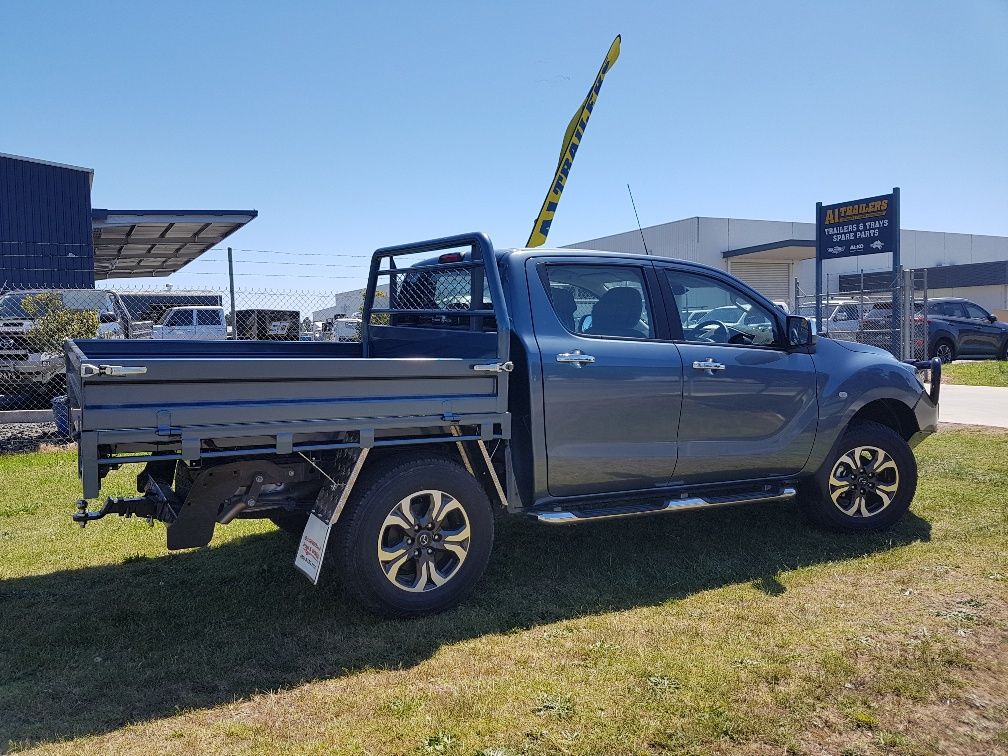 Dark gray pickup truck with a flatbed, parked on grass in front of a dealership on a sunny day.