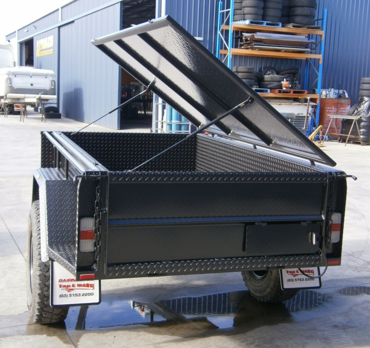 A black trailer with the lid open is parked in a parking lot