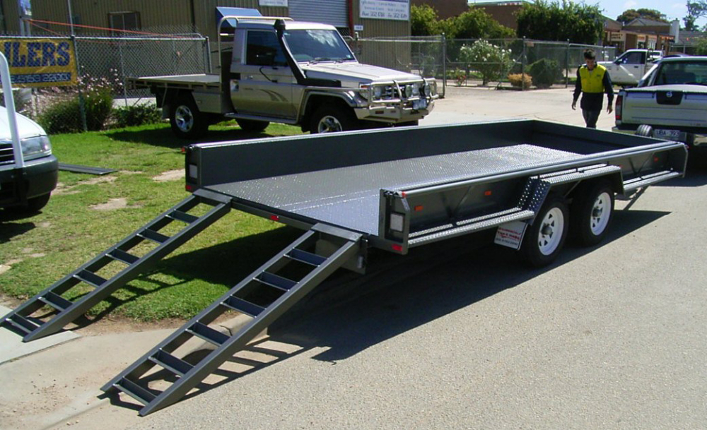 A trailer with ramps attached to it is parked on the side of the road