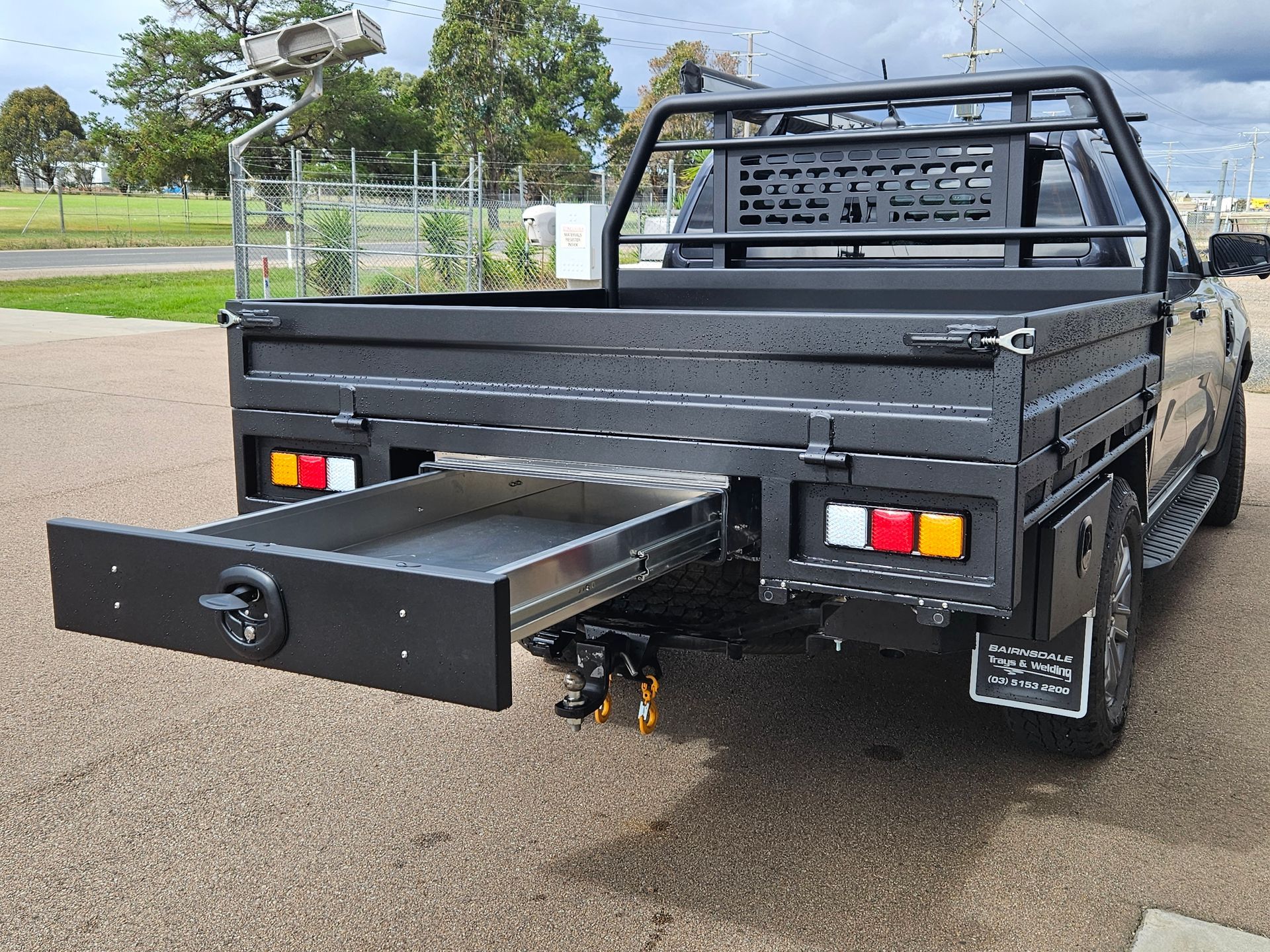 Black pickup truck with a pull-out drawer in the tray. It's parked outside on an asphalt surface.