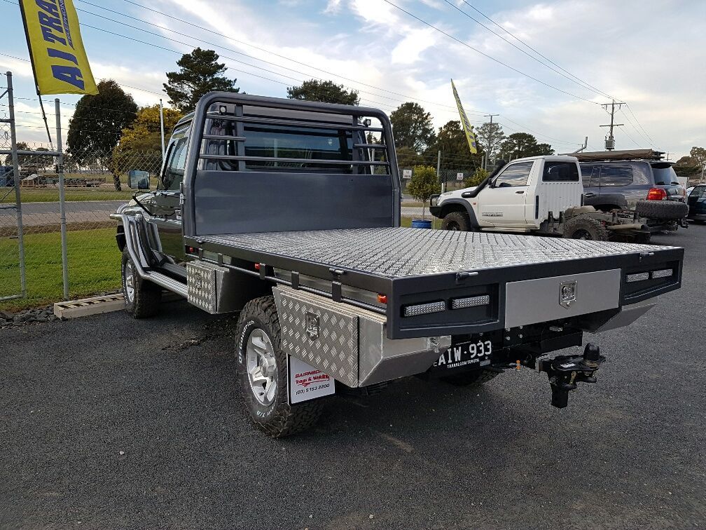 A flatbed truck with a black tray and aluminum accents parked on asphalt, displaying a license plate.