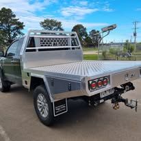 A utility truck with a flatbed, parked outdoors. The truck is gray with a silver flatbed, and the setting is a sunny day.
