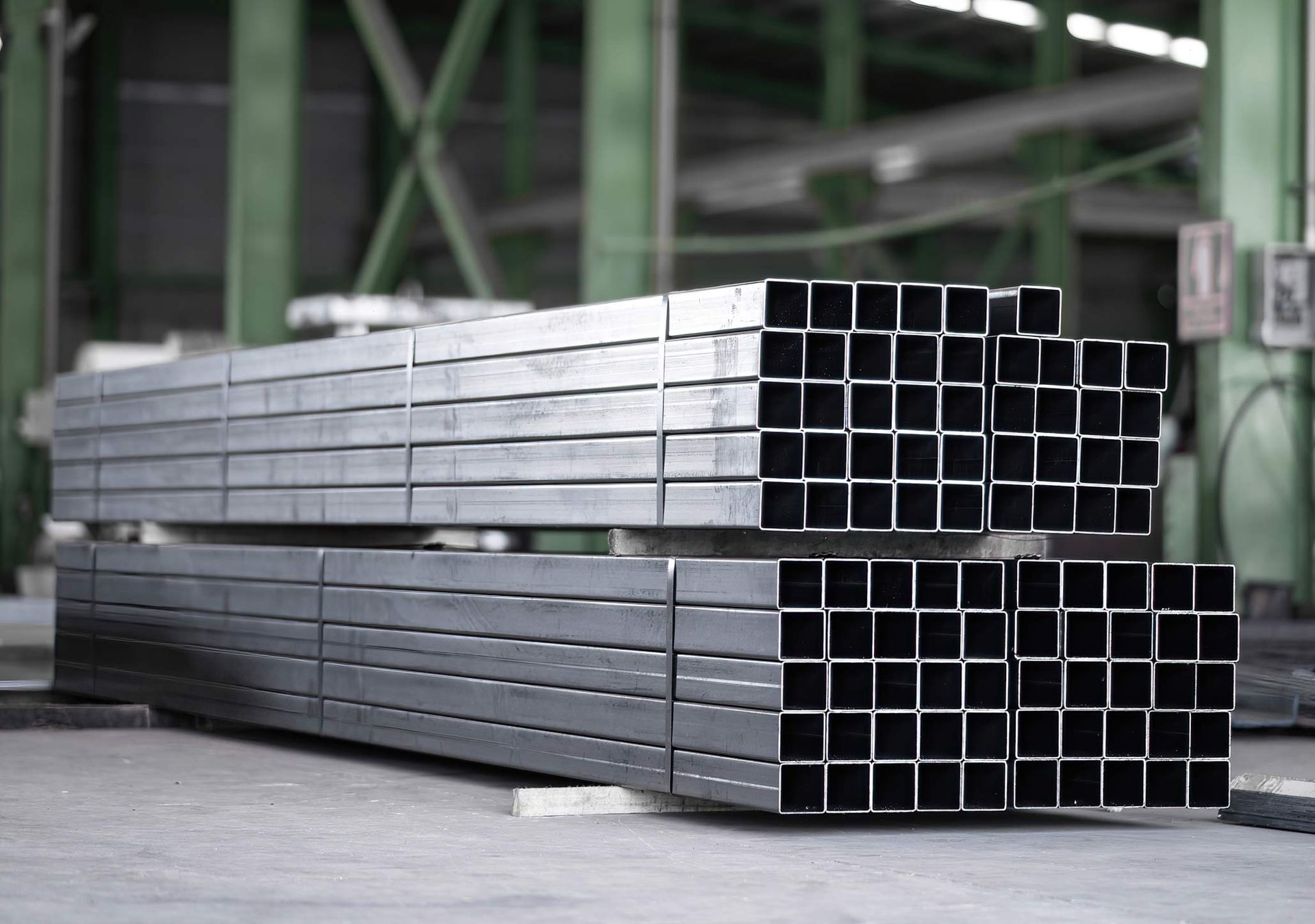 Stacked square tubes prepared for aluminium fabrication in industrial warehouse.