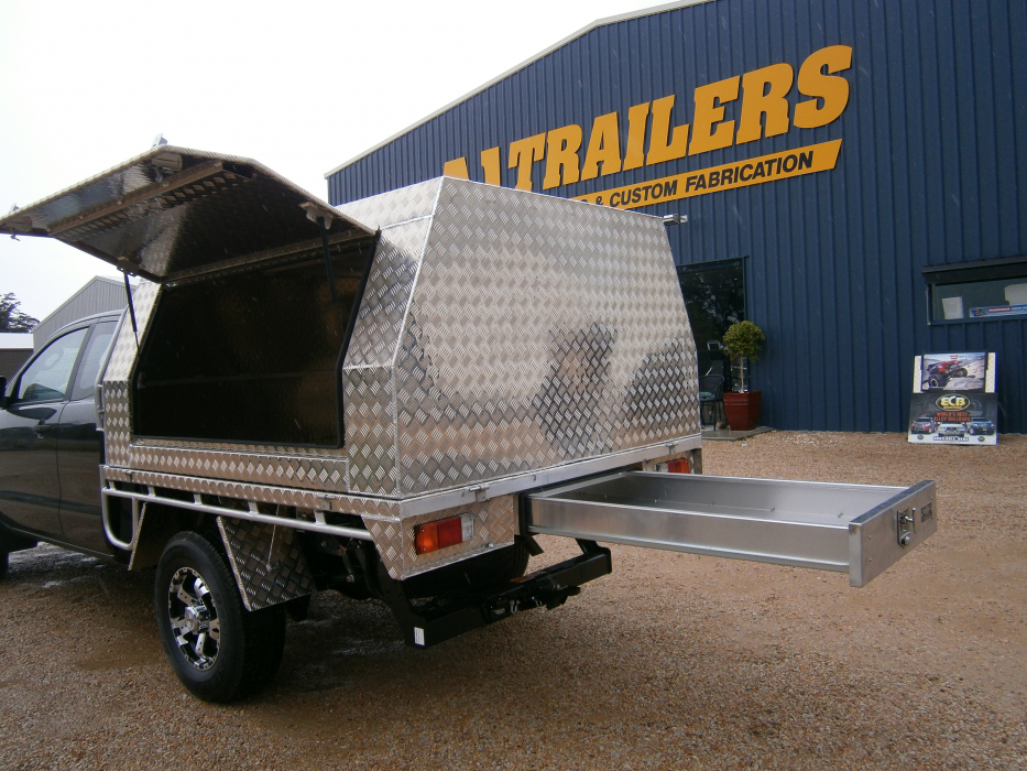 A truck with a canopy and drawers is parked in front of a trailers building.
