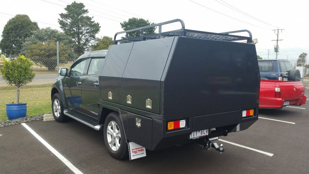 A black truck with a canopy is parked in a parking lot.