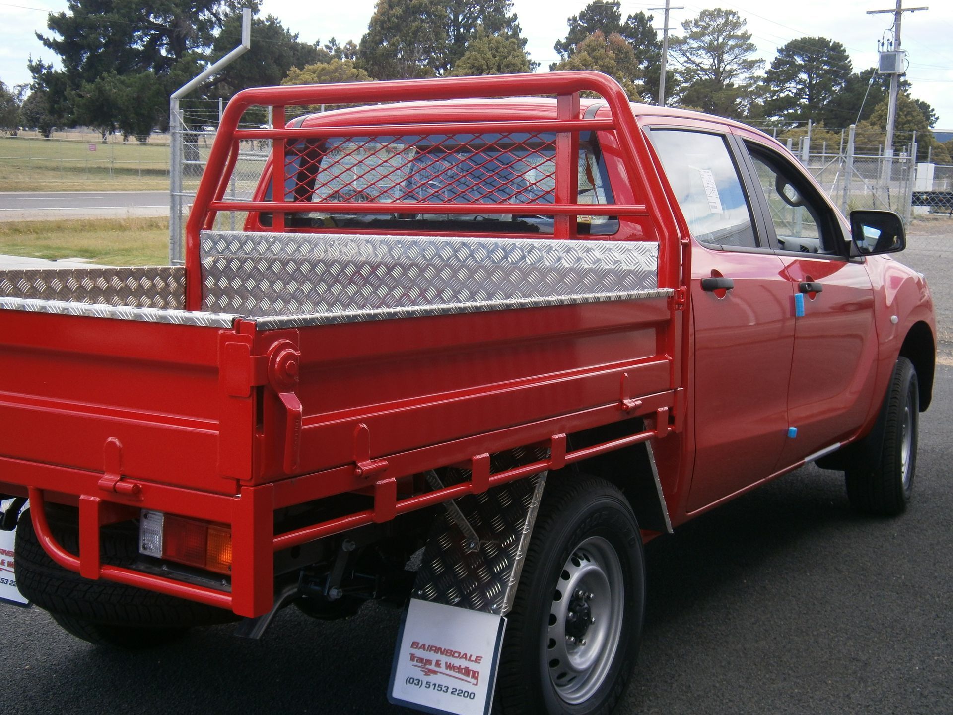 Red pickup truck with a custom metal tray bed and safety rack, parked outdoors on an overcast day.