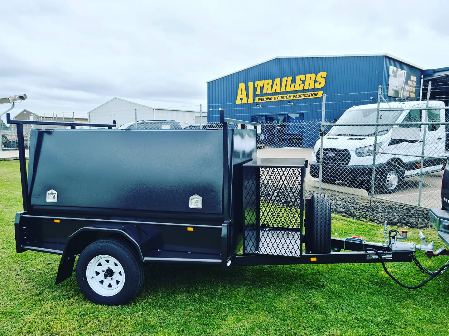 A black trailer is parked in front of a building that says a trailers.