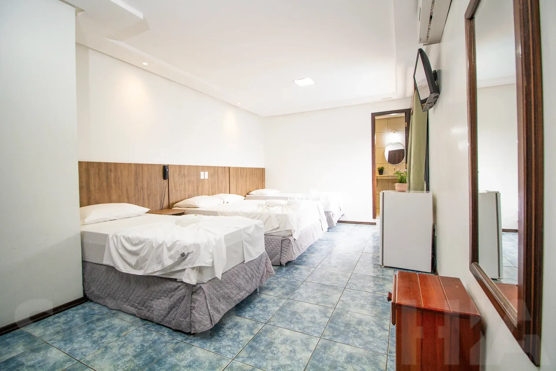 Quarto de hotel luminoso com duas camas de solteiro, carpete azul, paredes brancas e uma cômoda com espelho.