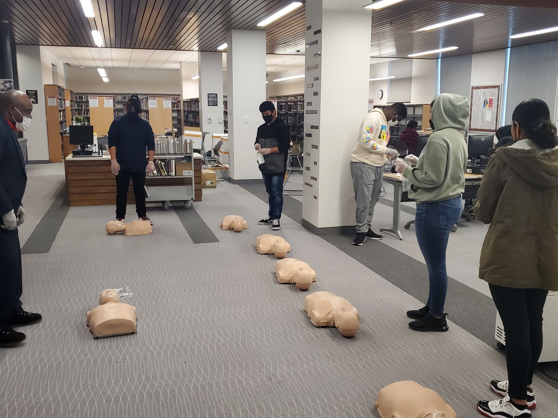 A group of people are standing around a row of cpr bags in a library.
