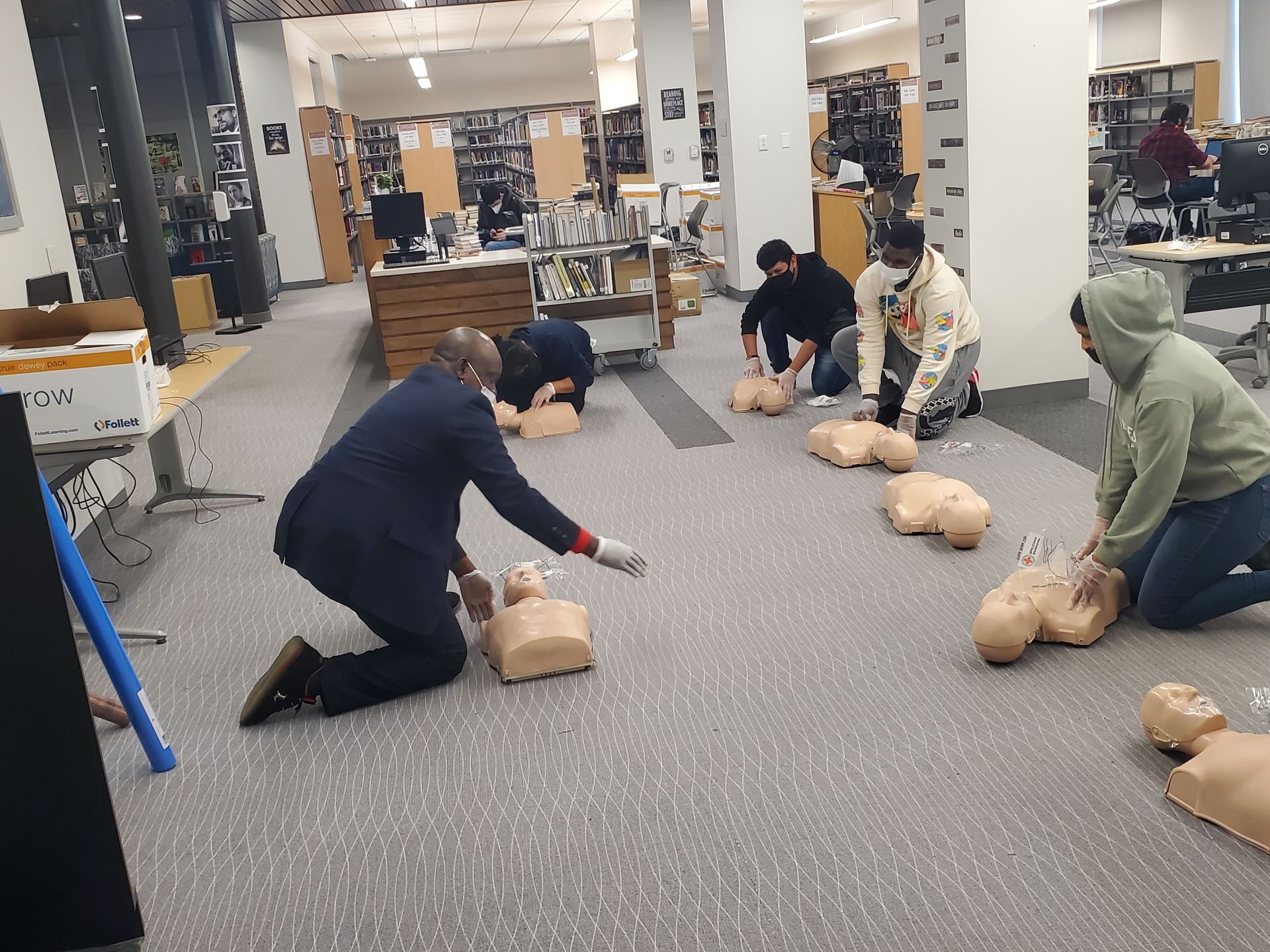 A group of people are practicing first aid on mannequins in a library.