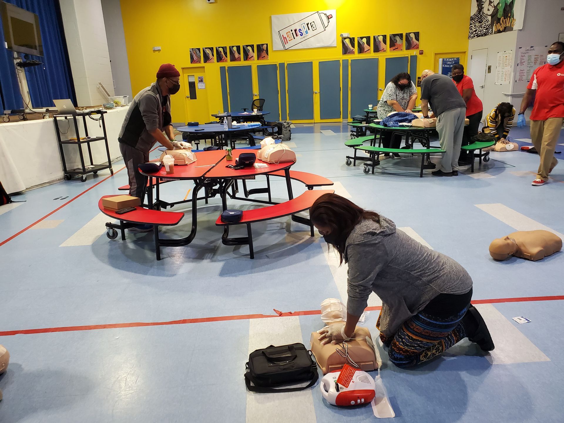 A group of people are practicing first aid on a mannequin in a gym.