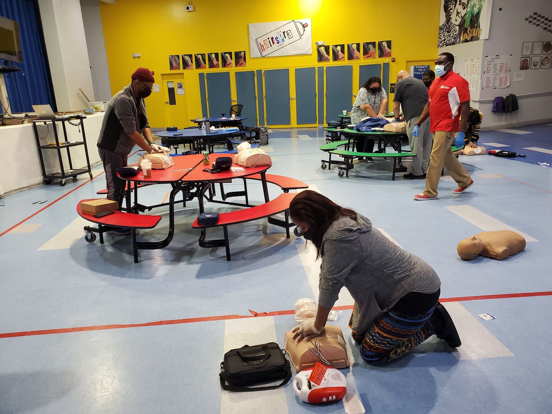 A woman is kneeling down in front of a mannequin in a gym.