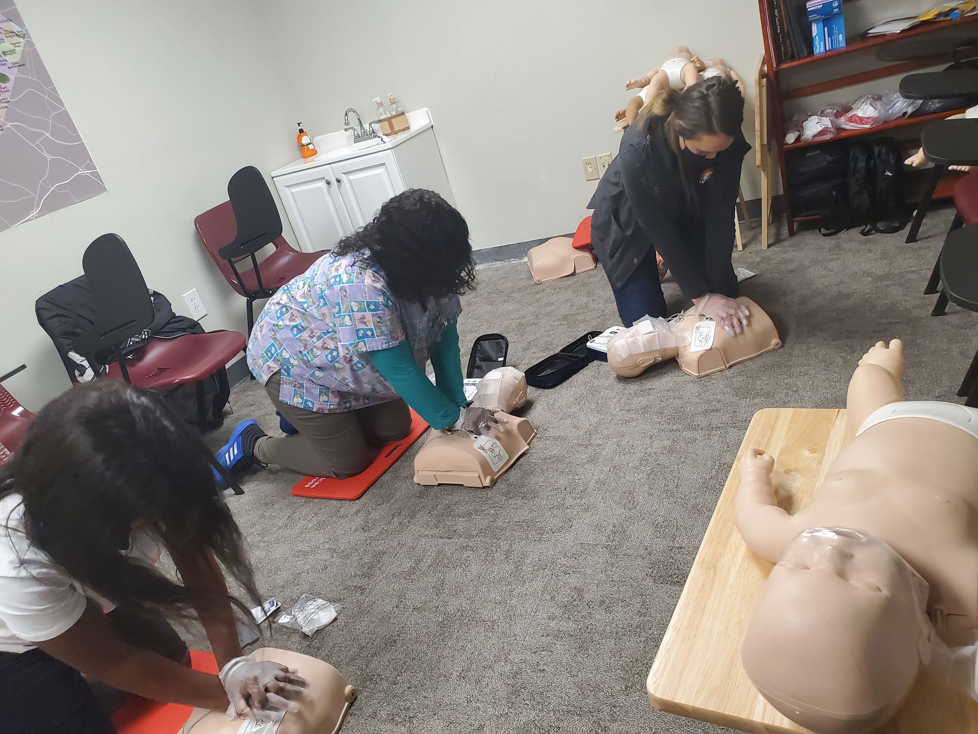 A group of women are practicing first aid on a baby mannequin.