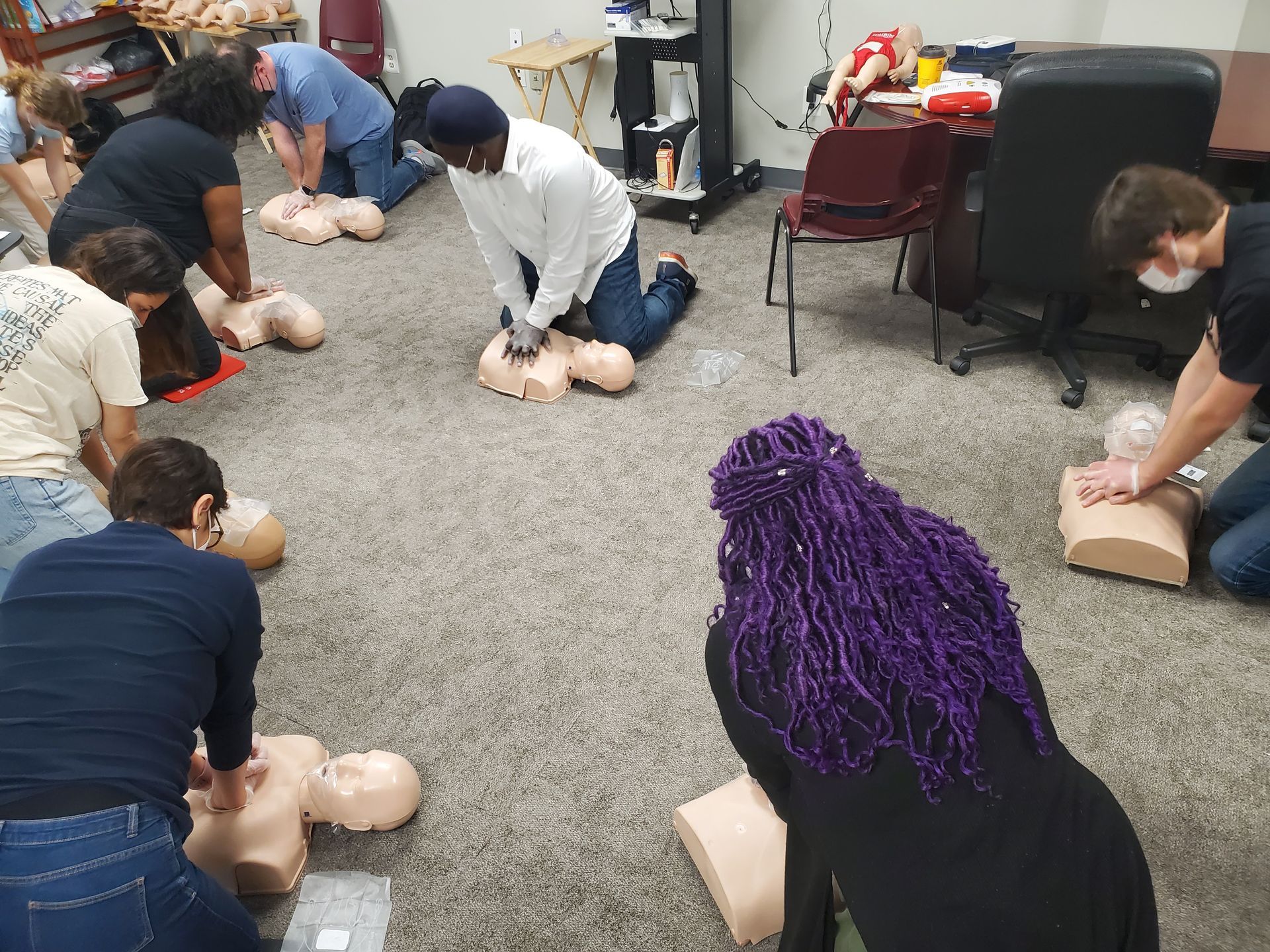 A group of people are practicing first aid on mannequins in a room.