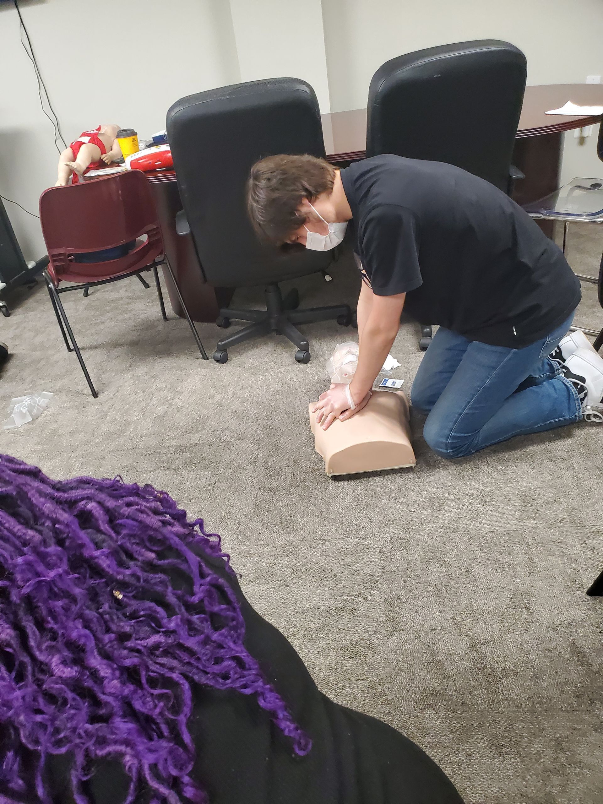 A man is kneeling down and doing a heart massage on a mannequin.