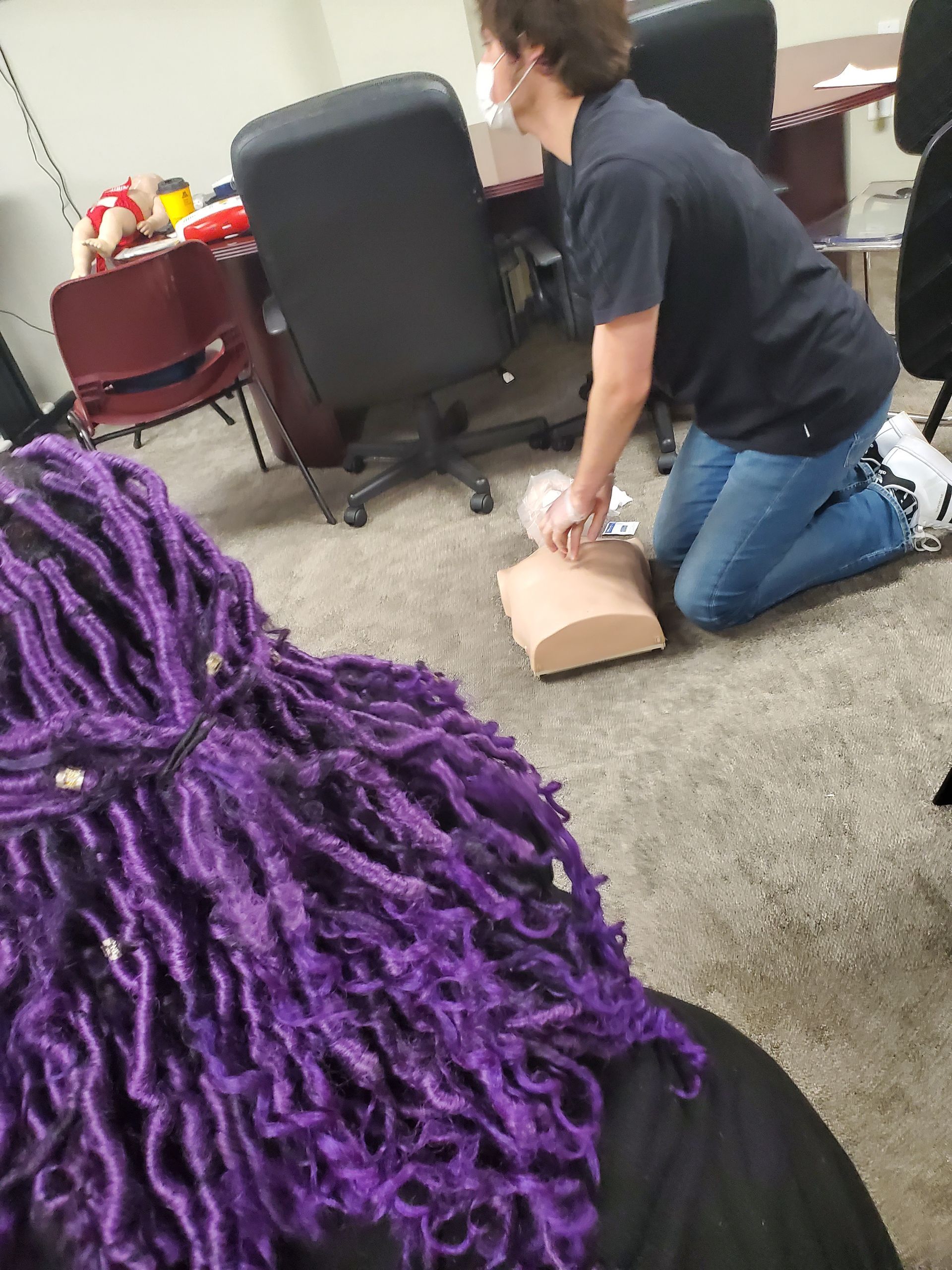 A man with purple dreadlocks is kneeling down in front of a mannequin.