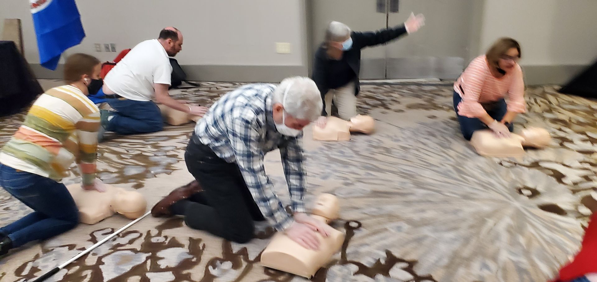 A group of people are kneeling on the floor doing a cpr on a mannequin.