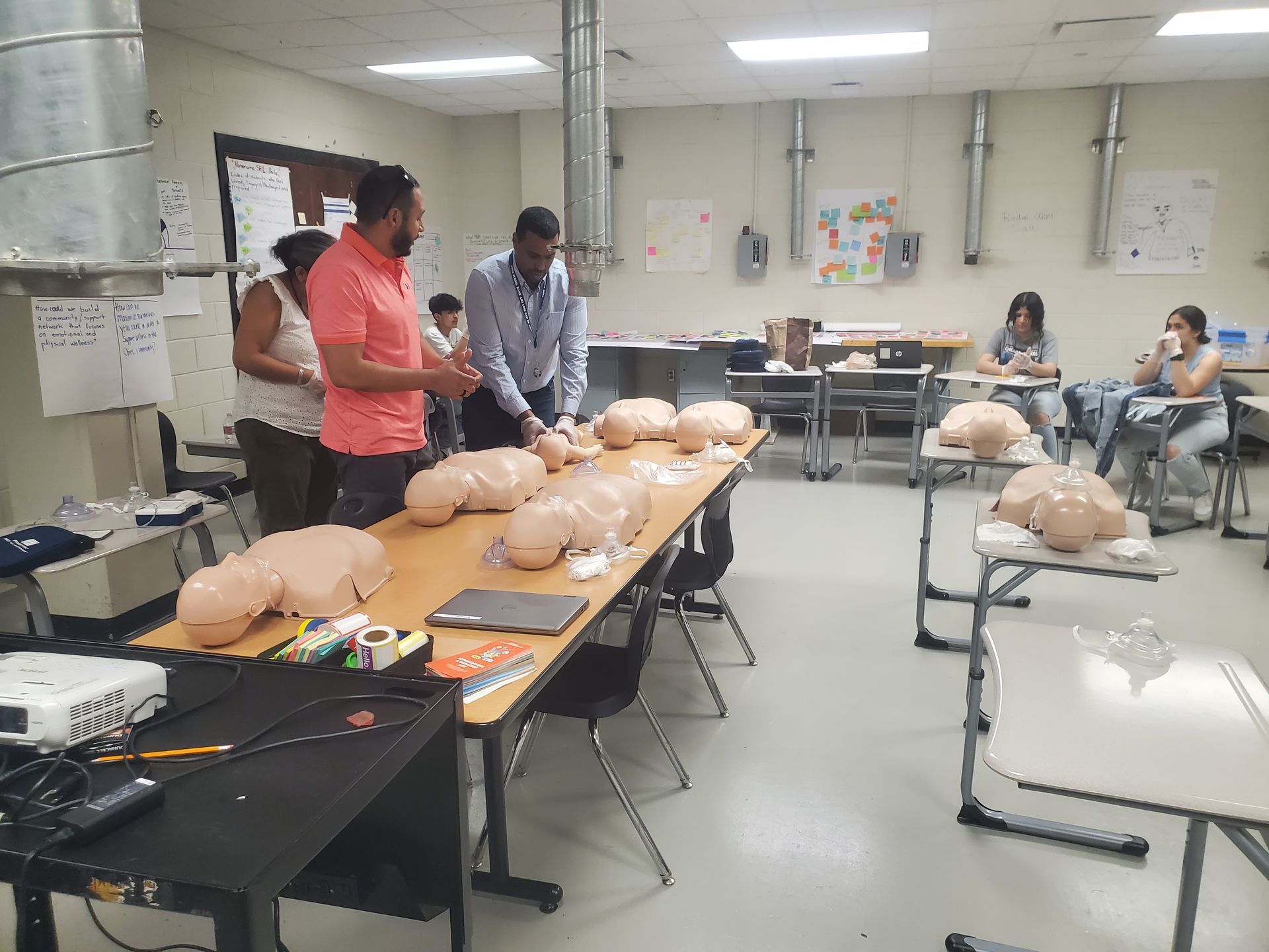 A group of people are standing around a table with mannequins on it in a classroom.