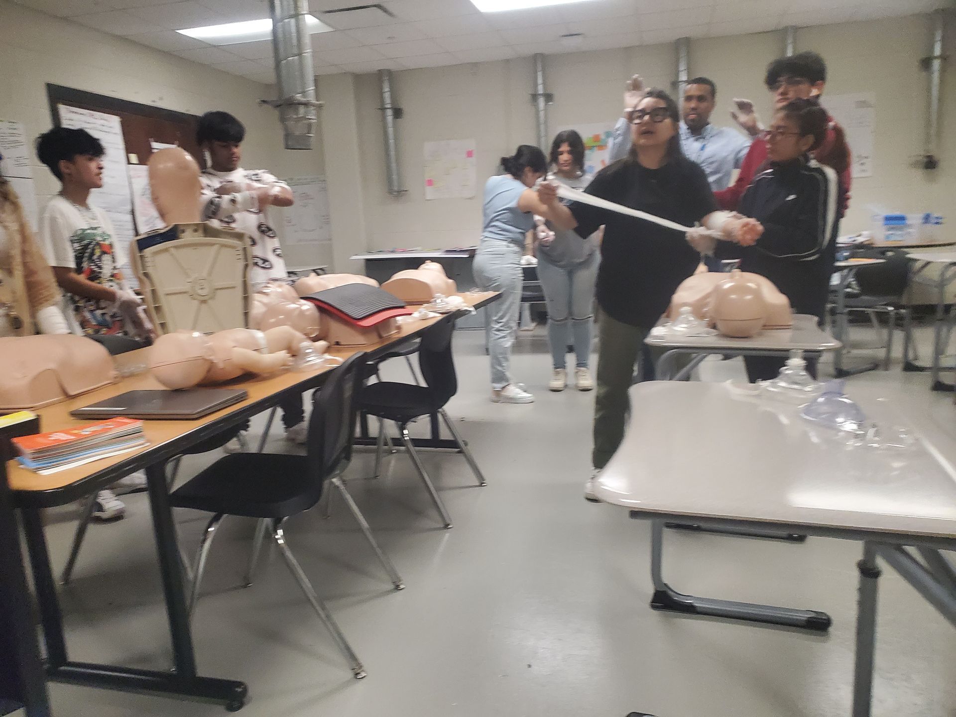 A group of people are standing around tables in a classroom.